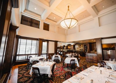 Landmark Tower Elegant restaurant interior with white tablecloths, dark wood furnishings, and a large chandelier under a coffered ceiling.