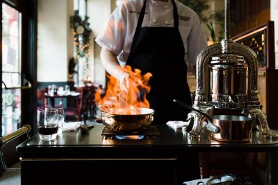 Landmark Tower Chef flambéing a dish at a restaurant table with a decorative espresso machine nearby.