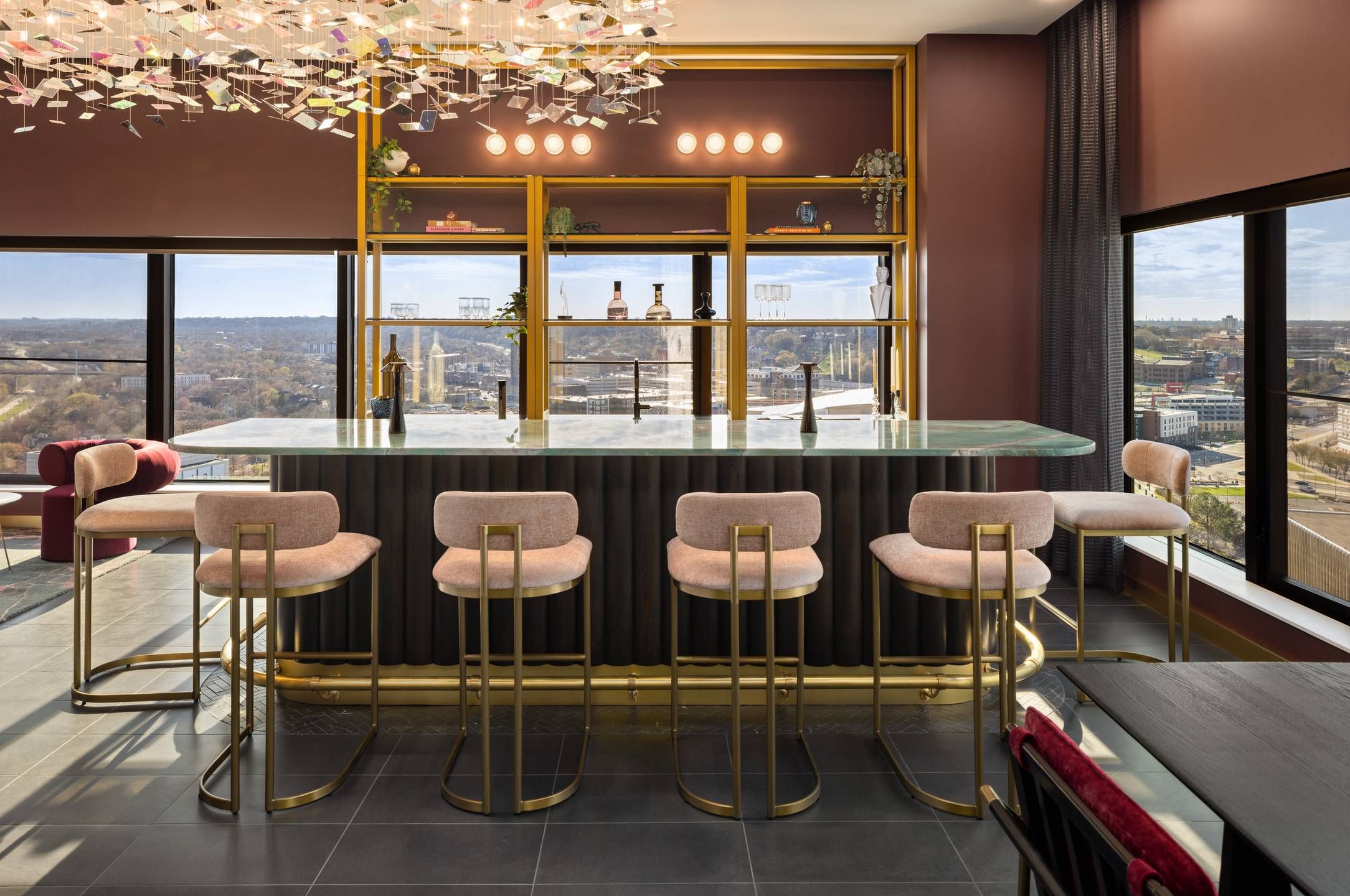 Landmark Tower apartments Modern bar with gold accents, six upholstered stools, marble countertop, and large windows with city views.