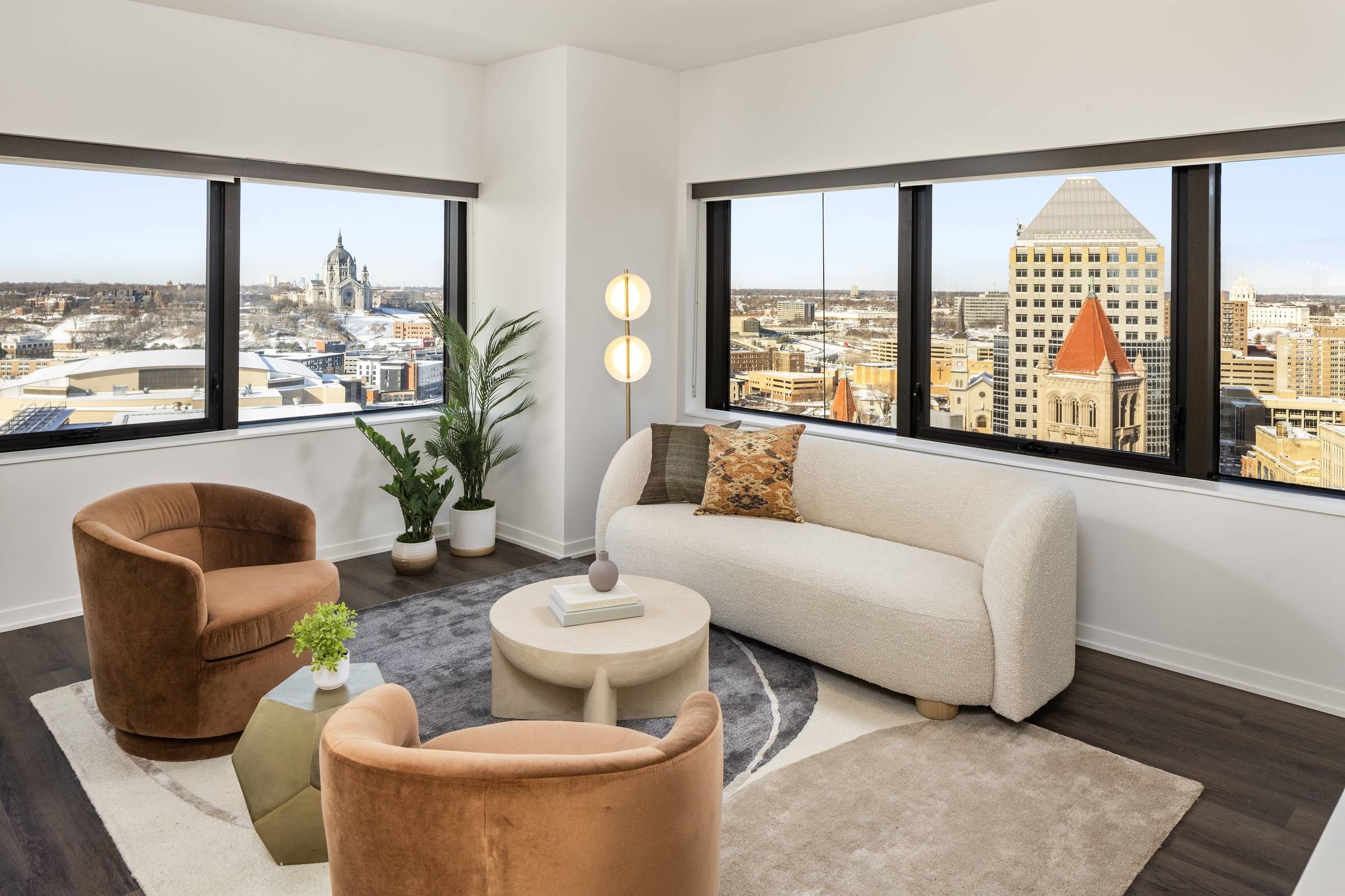 Landmark Tower Modern living room with city views, beige sofa, brown chairs, round table, plants, and large windows.