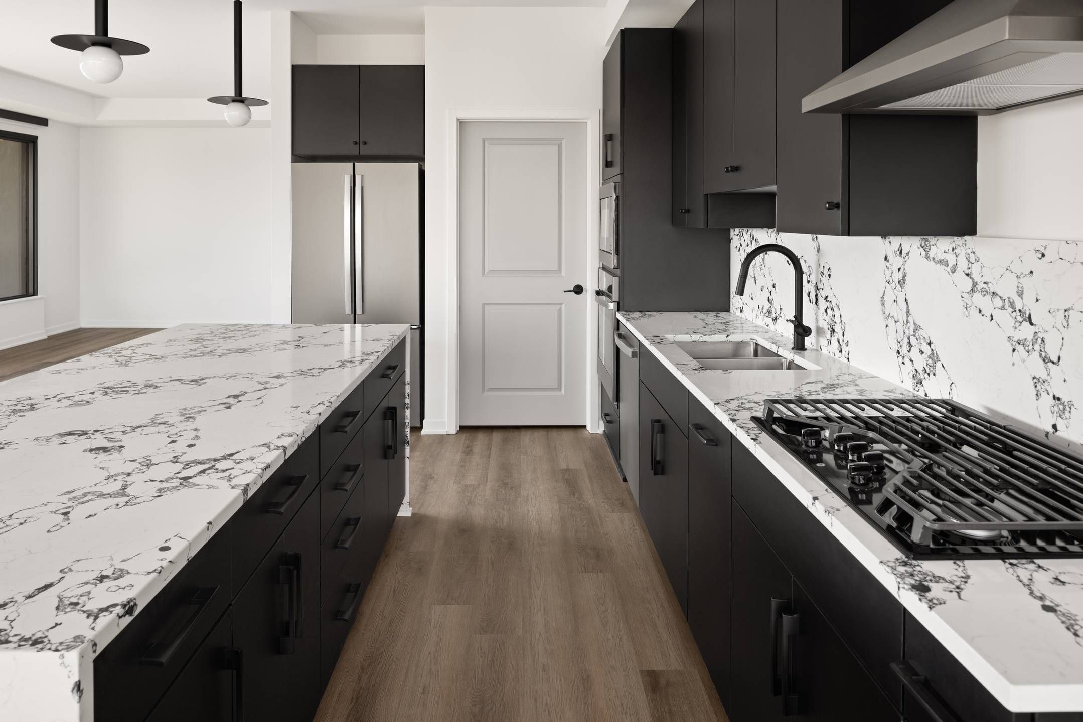Landmark Tower apartments Modern kitchen with black cabinets, white marble countertops, stainless steel appliances, and wood flooring.
