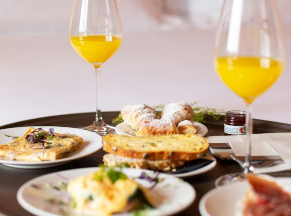 Breakfast tray with orange juice, pastries, toast, omelet, and small jar of jam on white plates.