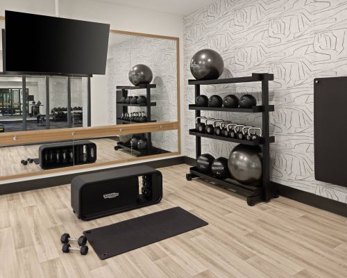 Landmark Tower apartments Modern gym room with exercise balls, kettlebells, a mat, dumbbells, mirror, and TV on a light wood floor.