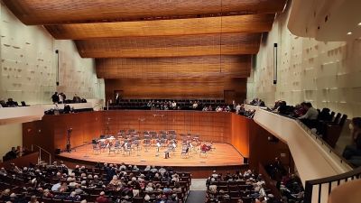 Landmark Tower Concert hall with an empty stage, surrounded by an audience seated in a tiered auditorium.