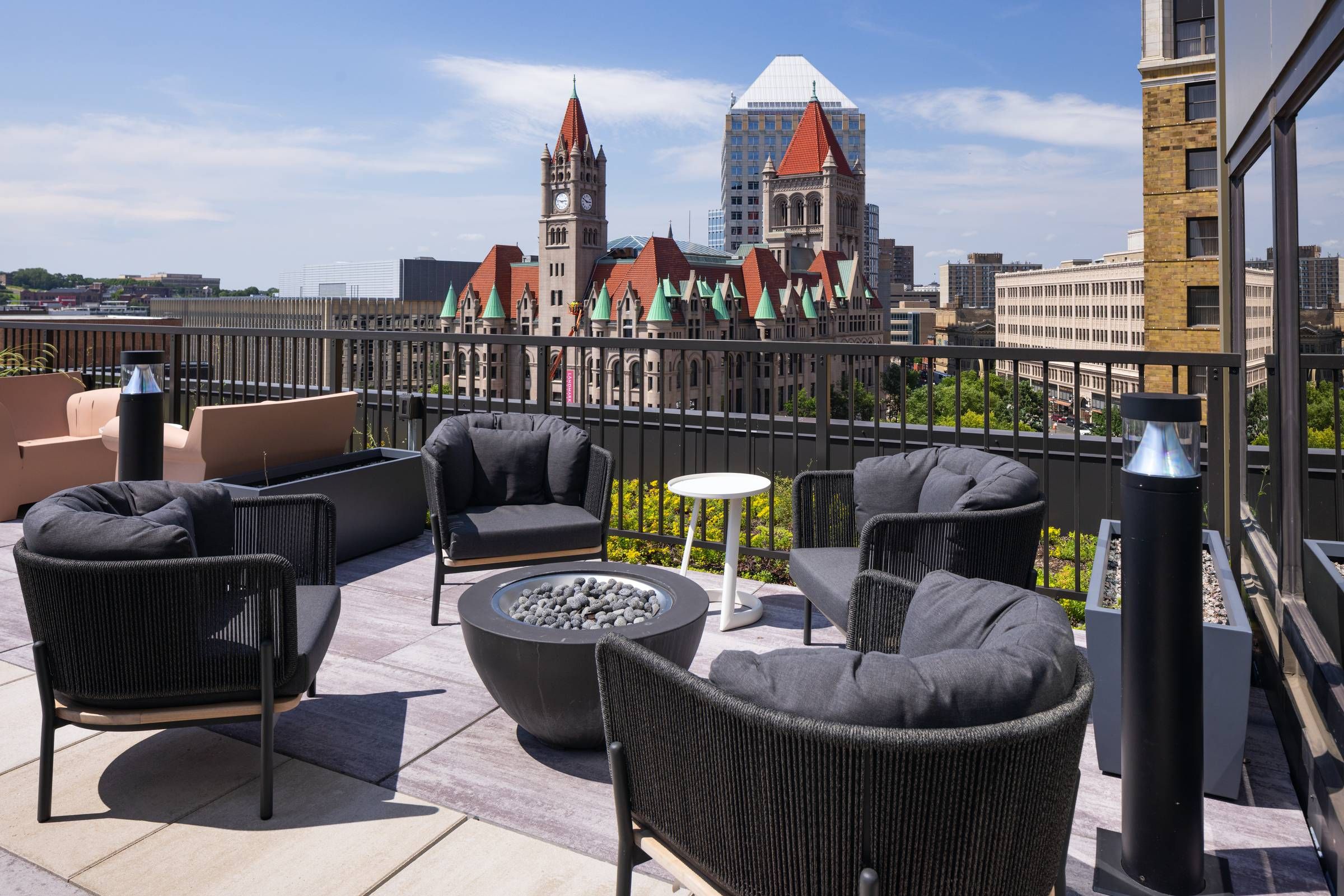 Outdoor rooftop lounge with modern seating, firepit, and view of historic and modern buildings under a blue sky.