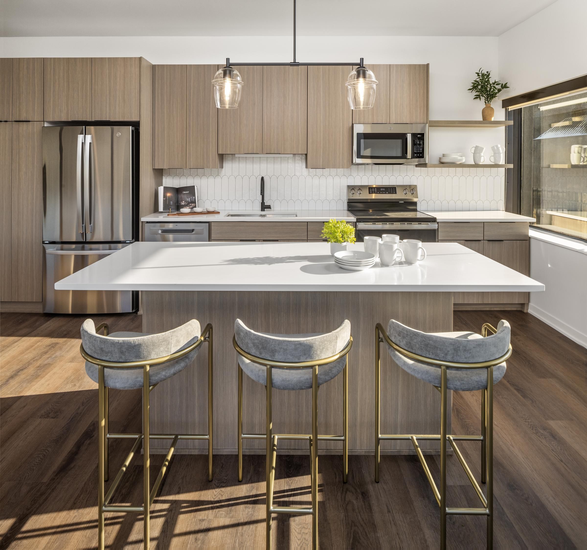 Landmark Tower Modern kitchen with wood cabinets, white countertops, pendant lights, and bar stools around an island.