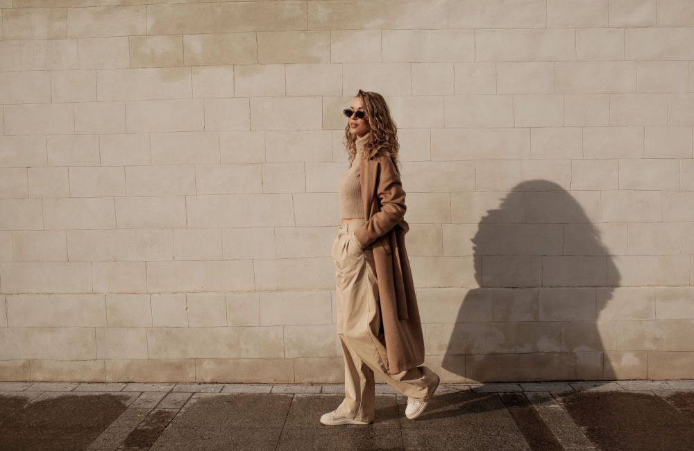 Landmark Tower Person in beige outfit and sunglasses walking along a sunlit brick wall.