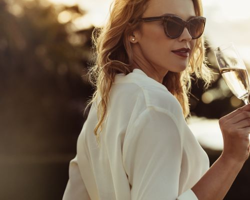 Landmark Tower Woman in sunglasses holding a glass of champagne, looking over her shoulder, with blurred background.
