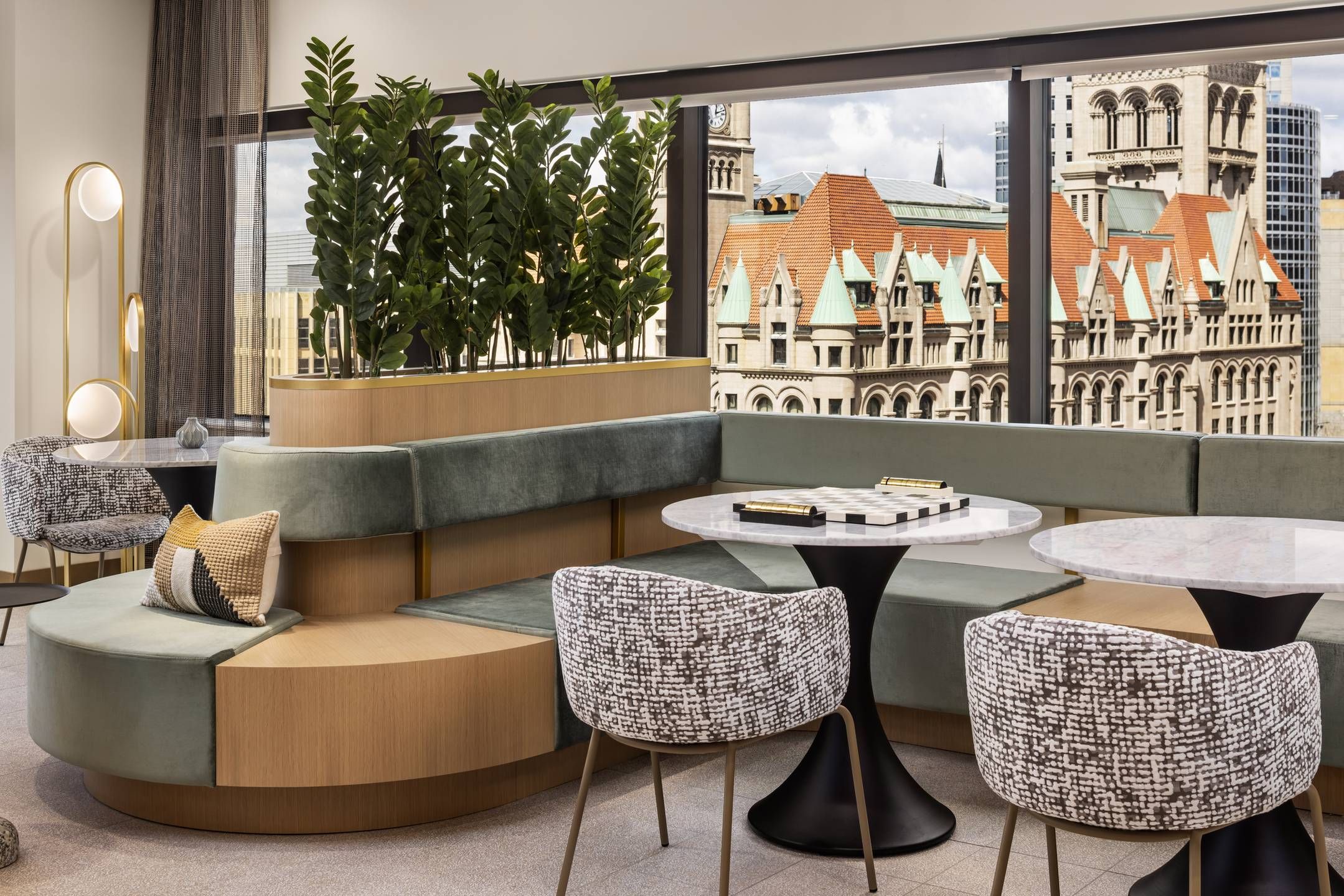 Landmark Tower apartments Modern lounge with curved green seating, potted plants, round marble tables, and cityscape view through large windows.