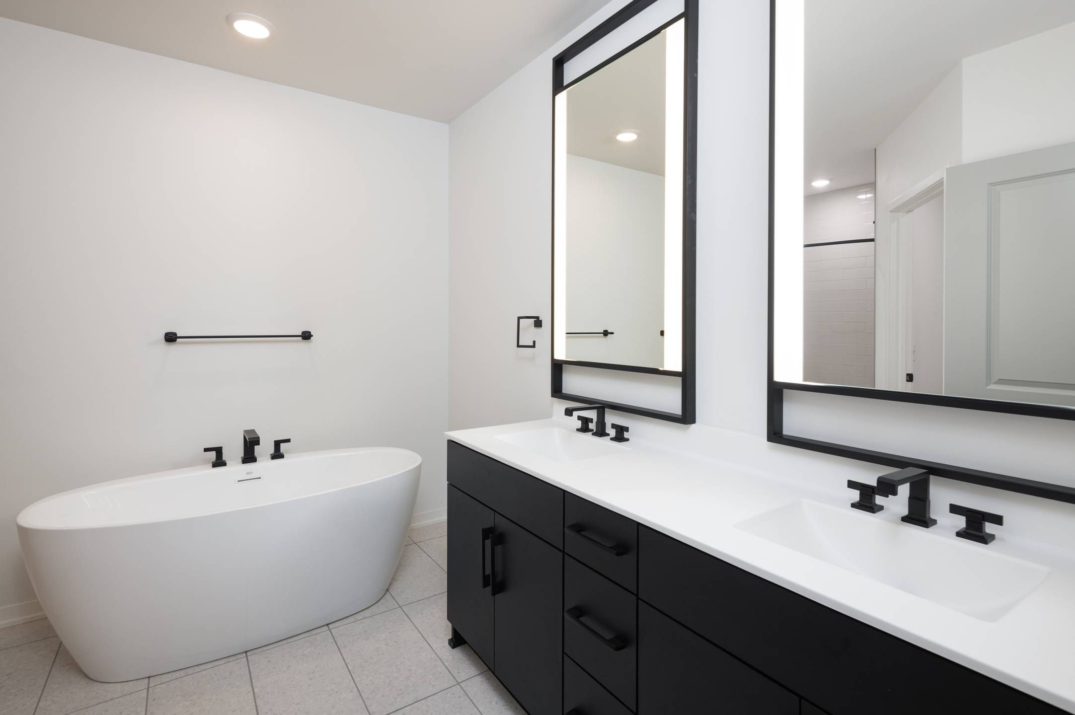 Landmark Tower apartments Modern bathroom with a white bathtub, double sink vanity, black fixtures, and large mirrors.