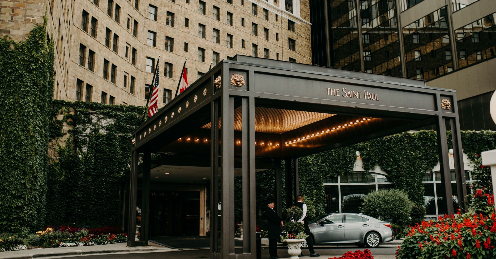 Landmark Tower Hotel entrance with "The Saint Paul" sign, flags, lit canopy, and greenery. A person stands near a parked car.