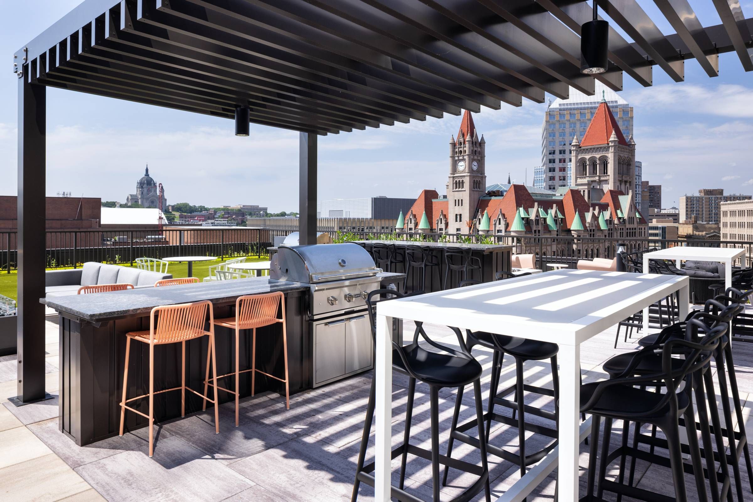 Modern rooftop patio with grill, high tables, and city views featuring historic buildings and a cathedral.