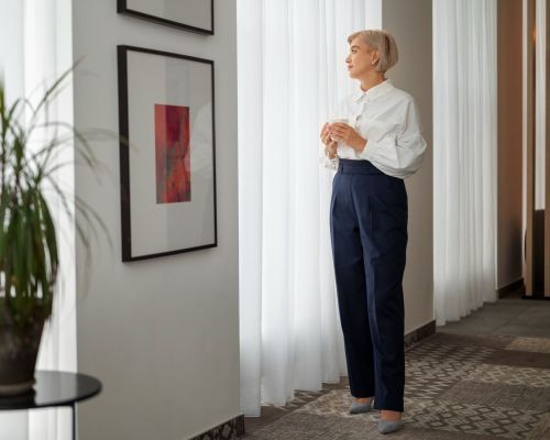 Landmark Tower A woman in a white blouse looks out a window, standing near framed art and a potted plant.