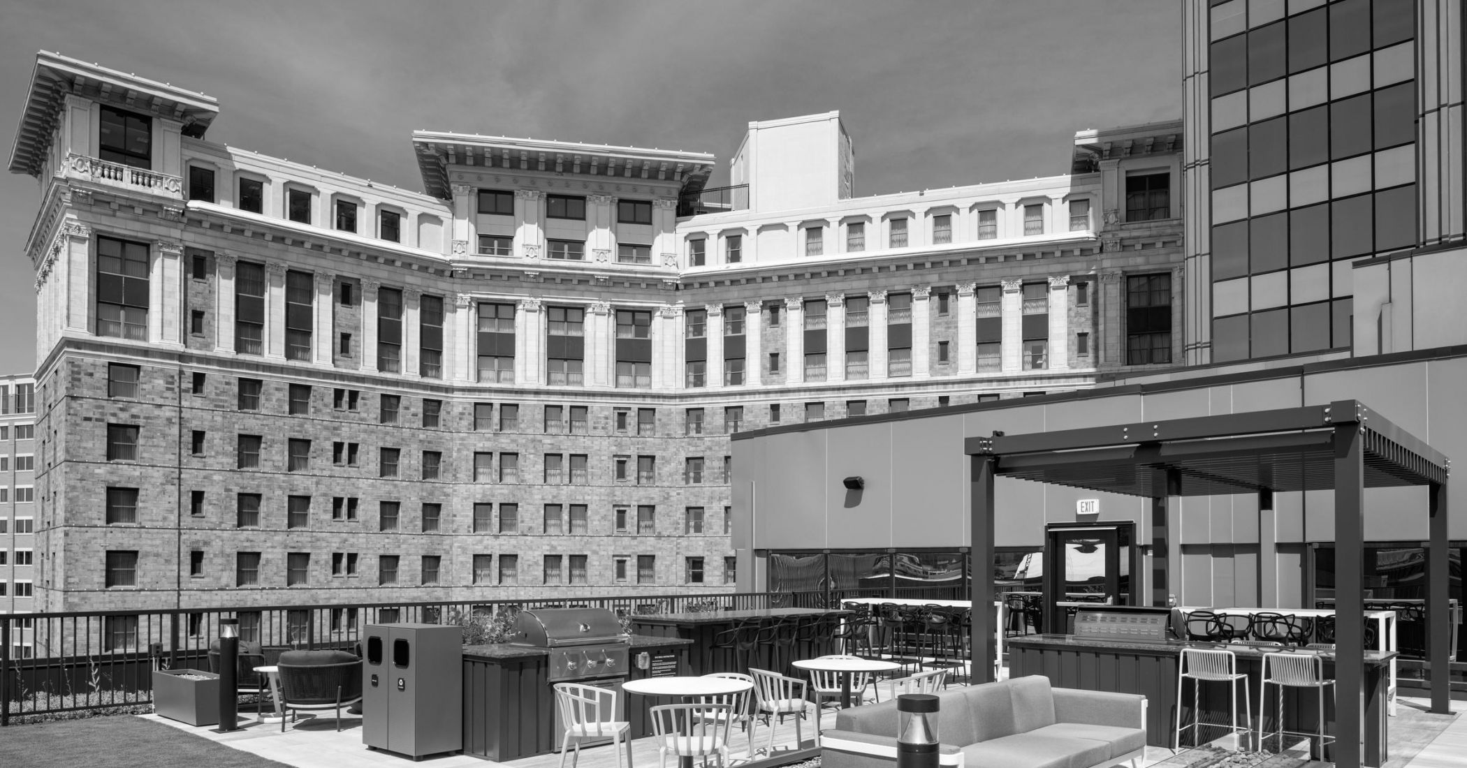 Rooftop patio with modern seating, tables, and pergola, set against a large historic building.