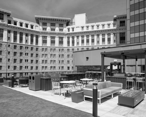 Rooftop patio with modern seating, tables, and pergola, set against a large historic building.