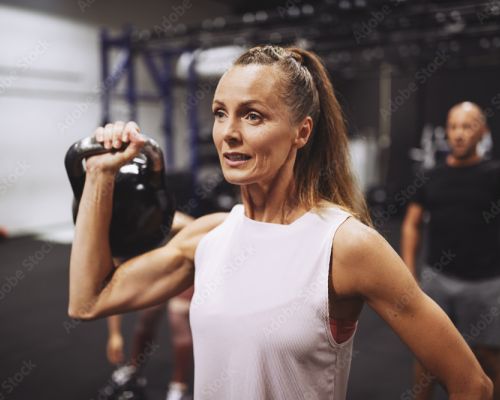 Woman holding a kettlebell in a gym, performing a strength exercise with focus and determination.