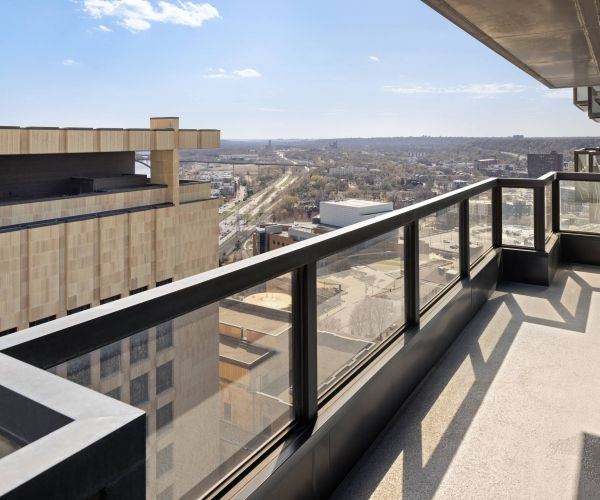 Landmark Tower apartments penthouse high-rise balcony with glass railing, overlooking city buildings and a distant, clear skyline.