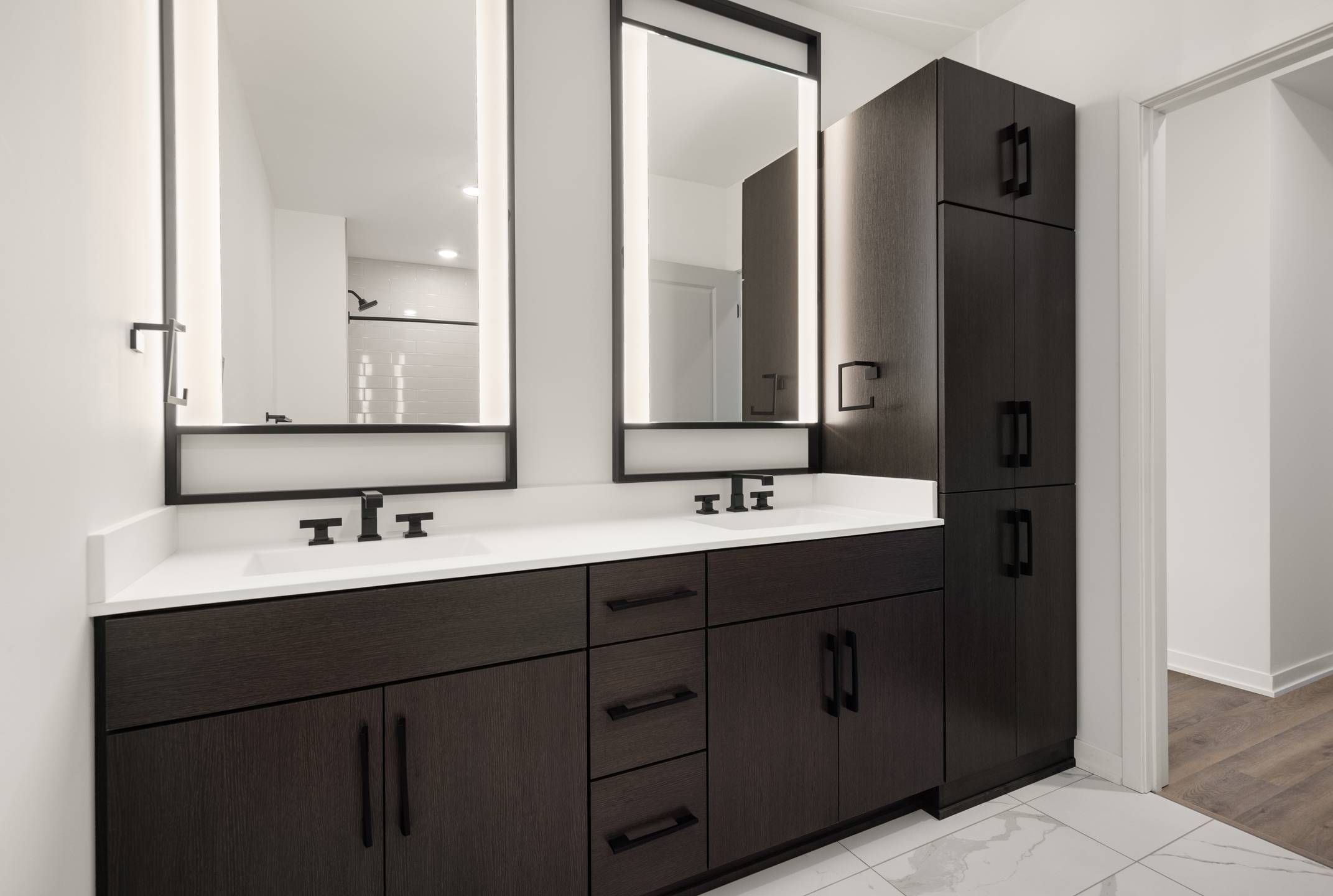 Landmark Tower apartments Modern bathroom with double vanity, dark cabinets, large mirrors, and white tile floor.