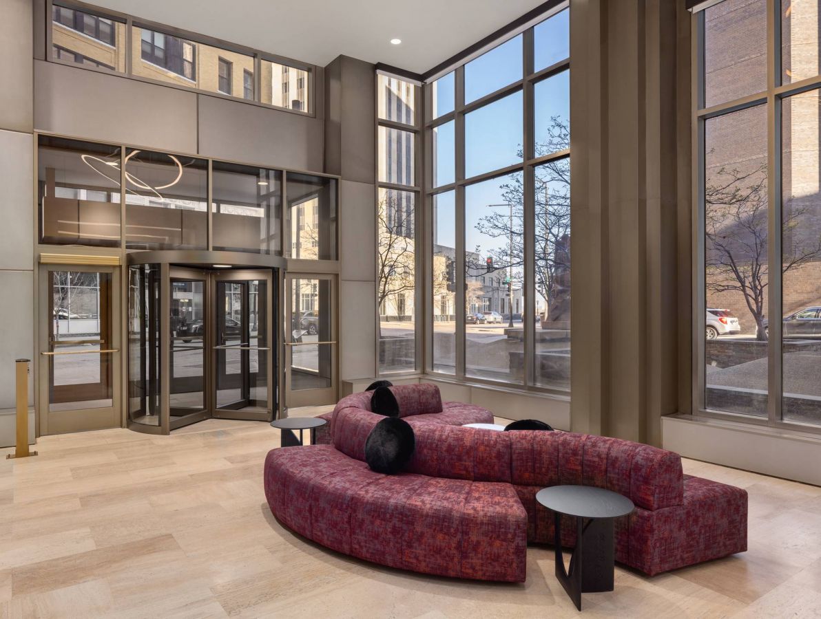 Landmark Tower apartments Modern lobby with curved red sofa, black pillows, round tables, large windows, and glass entrance doors.