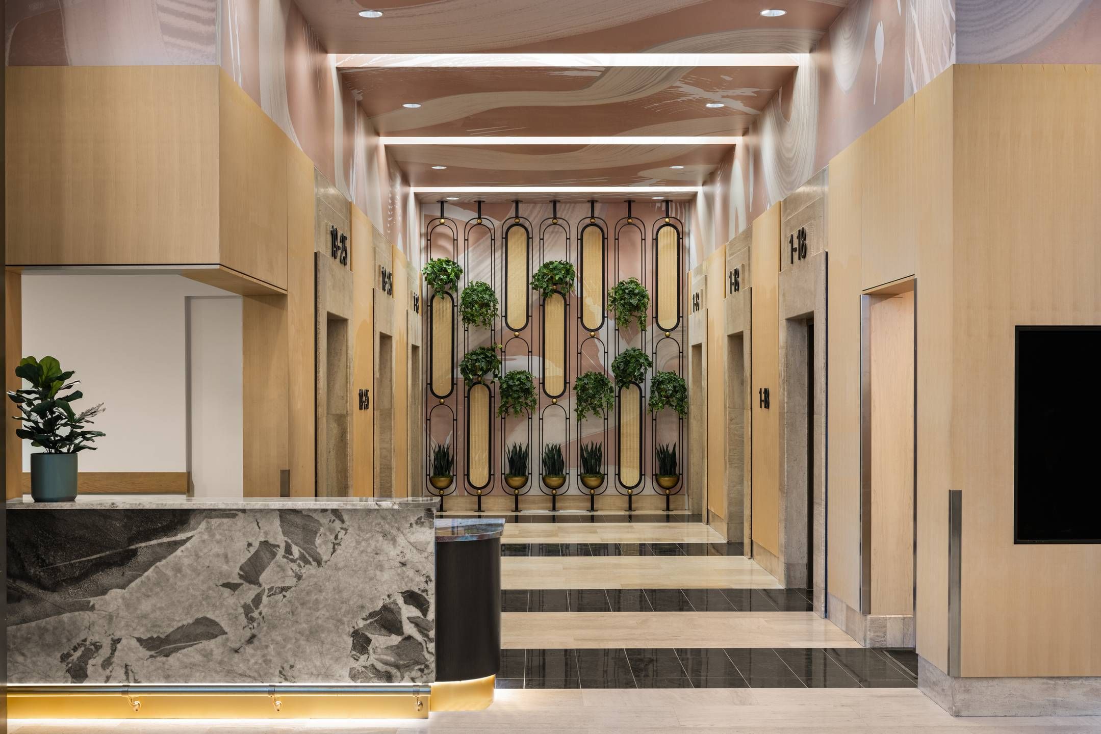 Landmark Tower apartments Modern elevator lobby with light wood paneling, marble reception desk, and wall-mounted potted plants.