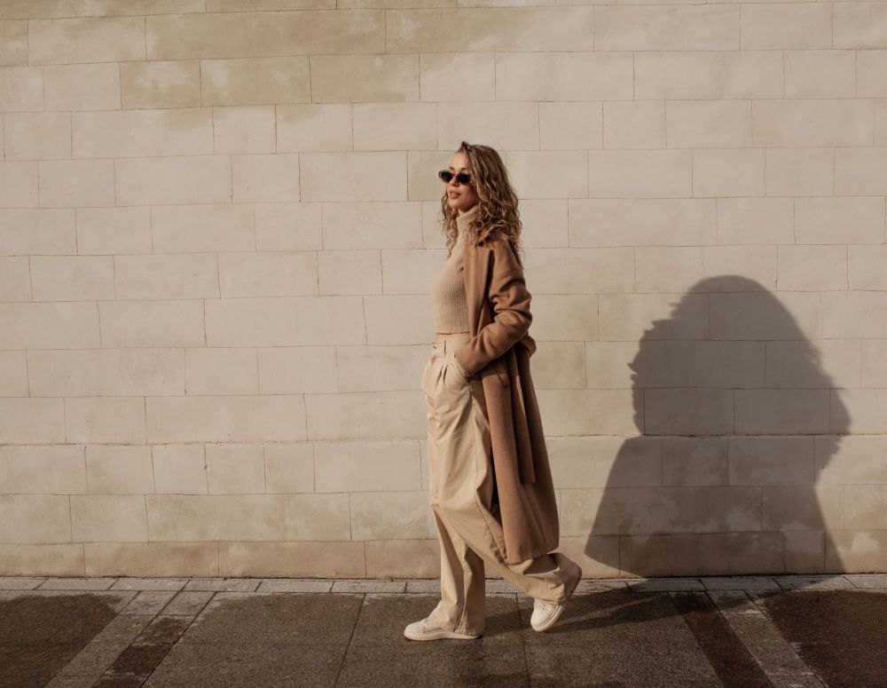 Landmark Tower Person in beige outfit and sunglasses walking along a sunlit brick wall.