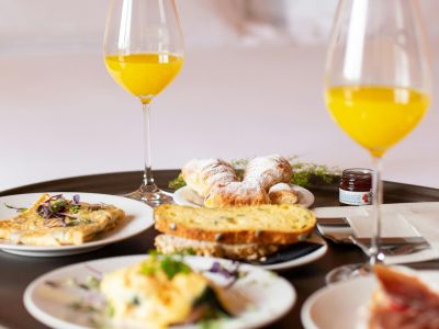 Breakfast tray with orange juice, pastries, toast, omelet, and small jar of jam on white plates.